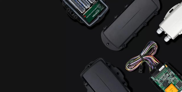 Battery-powered IoT tracking devices and electronic components on a black background, showcasing rugged GPS and telematics hardware for asset monitoring.