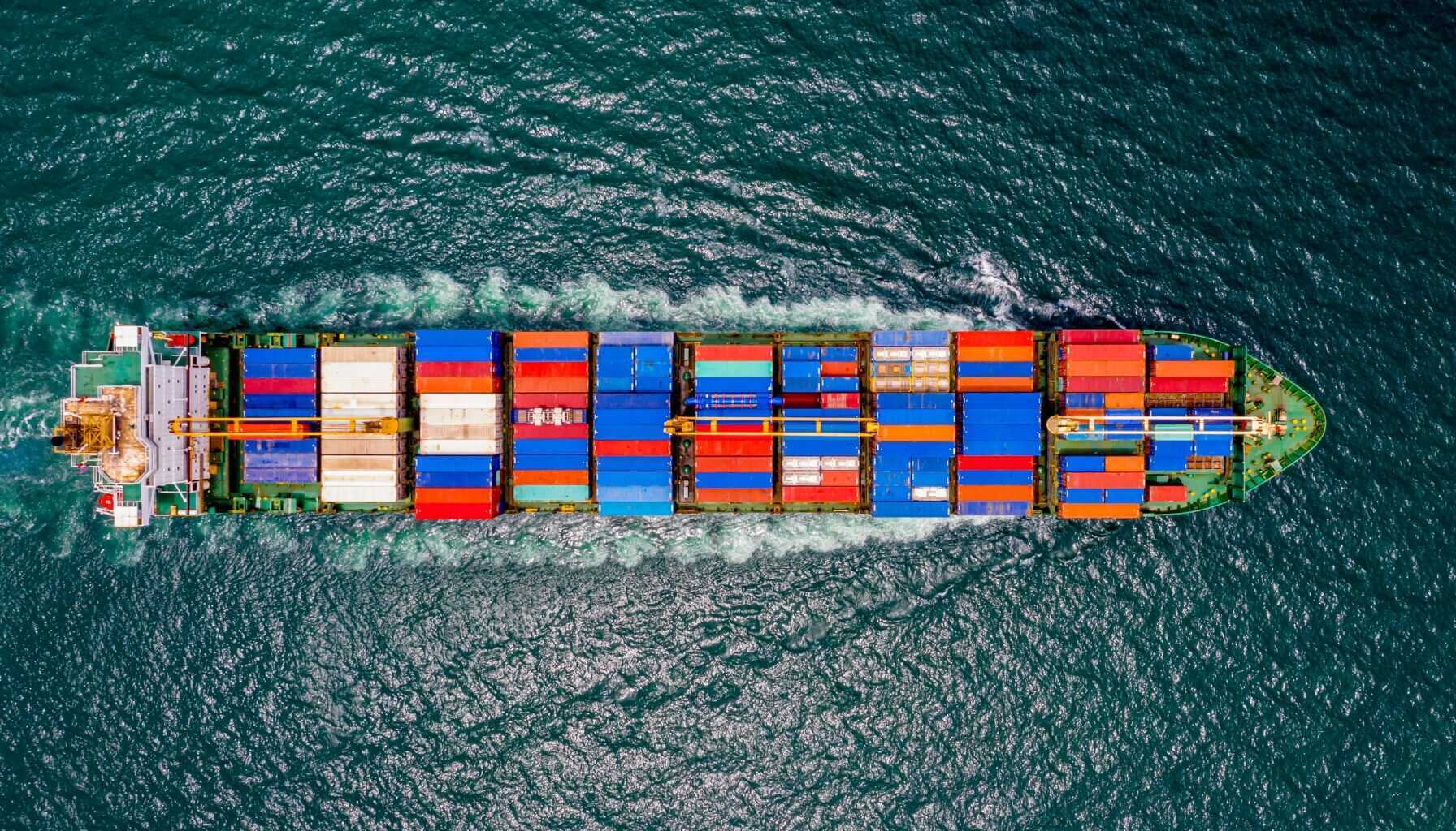 Aerial view of a large cargo ship carrying colorful shipping containers across the ocean, representing global logistics, maritime transport, and asset tracking solutions.