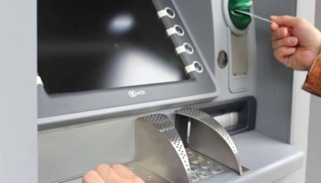 Person using an ATM machine, inserting a card into the slot, representing financial asset monitoring and IoT security solutions for banking equipment.