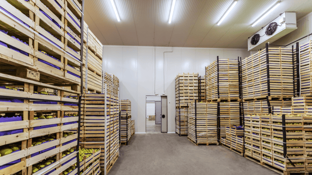 Cold storage warehouse with stacked wooden crates of produce, illustrating cold chain temperature monitoring and refrigerated asset management solutions.