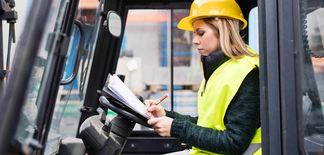 Female construction worker in a high-visibility vest and hard hat reviewing documents inside a vehicle, representing in-vehicle monitoring systems (IVMS) and driver safety management.