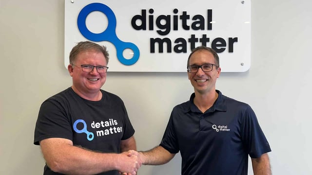 Two Digital Matter team members shaking hands in front of the company logo, representing partnership, collaboration, and IoT technology leadership.